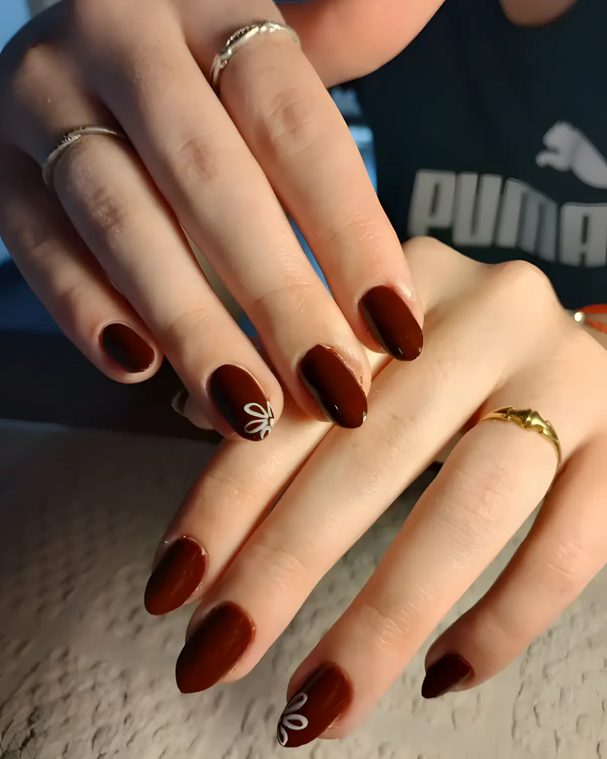 Uñas color chocolate con una florcita blanca pintada a pincel