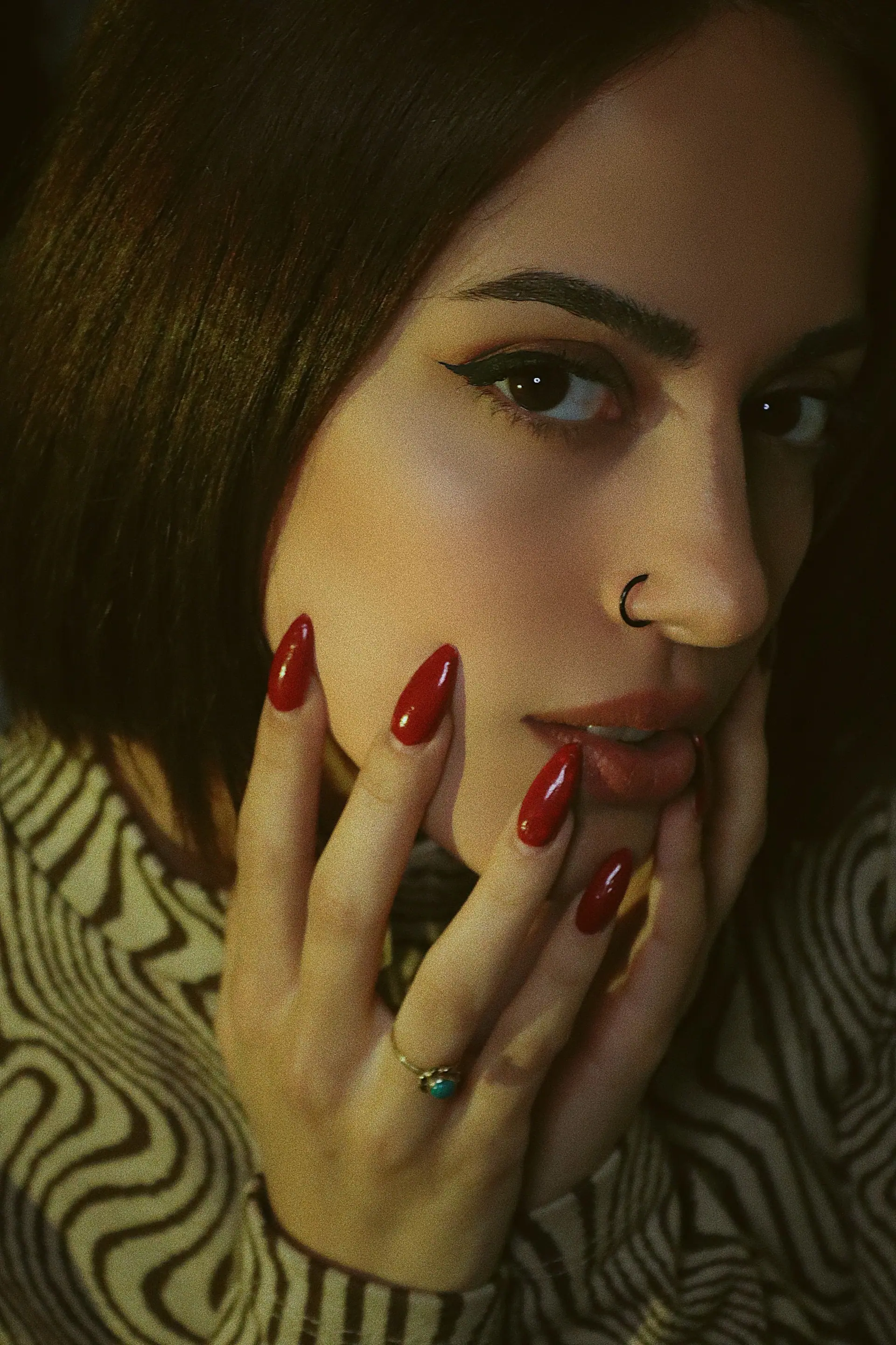 Modelo con uñas rojas almendradas apoyando la mano en el rostro (imagen de archivo)